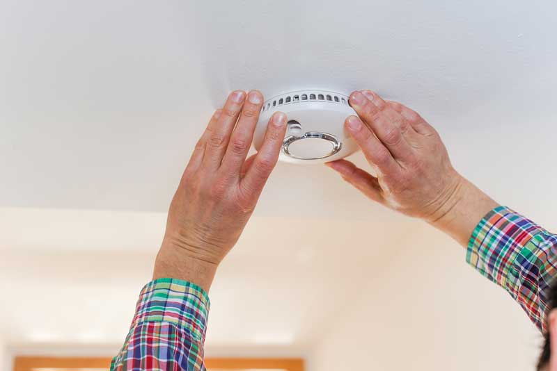 Person bringt Rauchmelder an der Decke an